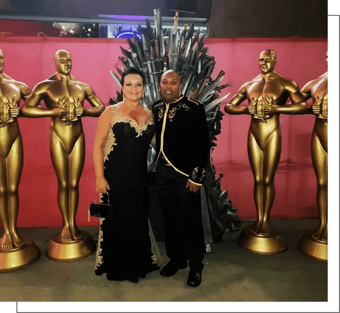 A man and woman posing in front of the iron throne.